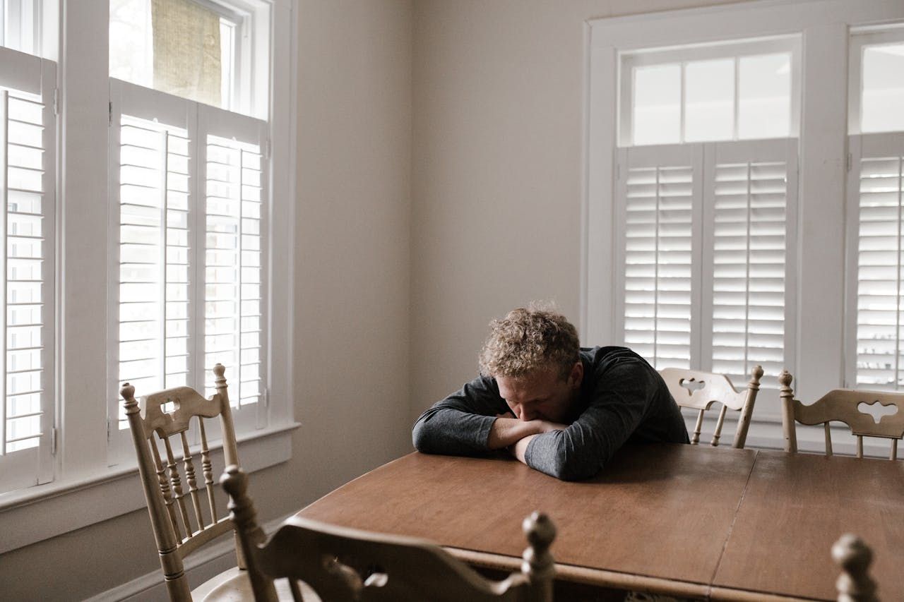 A man sitting alone with his head down, appearing overwhelmed and stuck in thought.