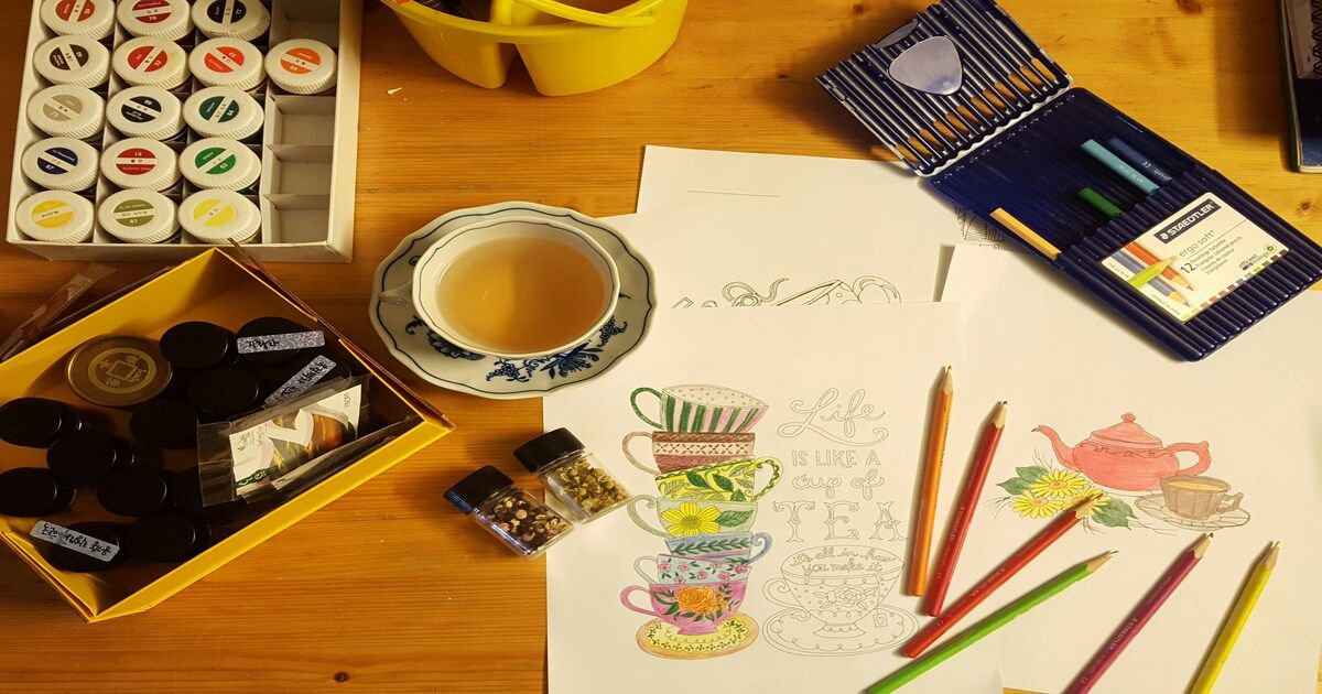 Coloring pages, colored pencils, paints, and a cup of tea on a wooden desk showing how creative hobbies help reduce stress and improve mental health.