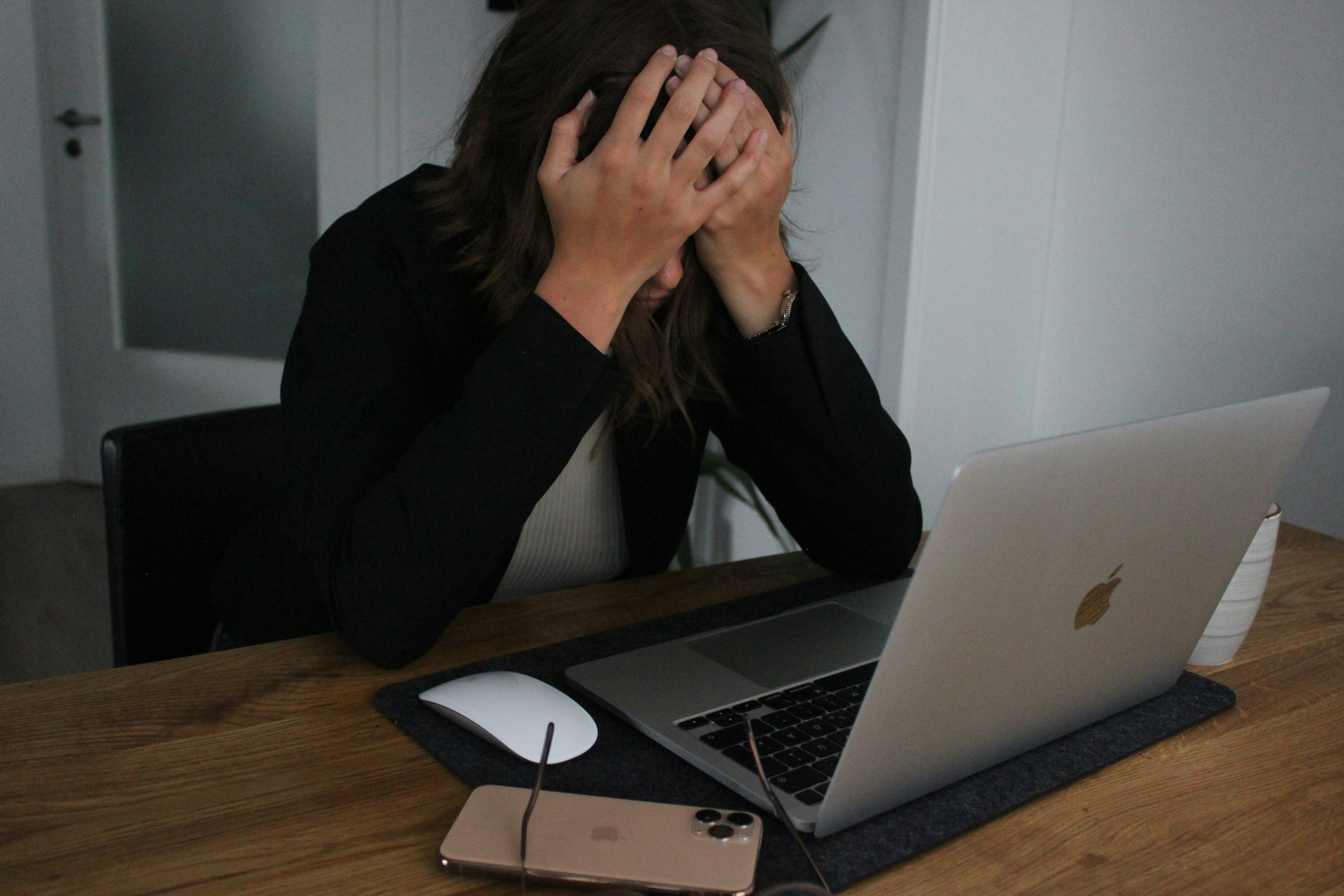 Stressed person sitting at a desk with head in hands, laptop in front, overwhelmed