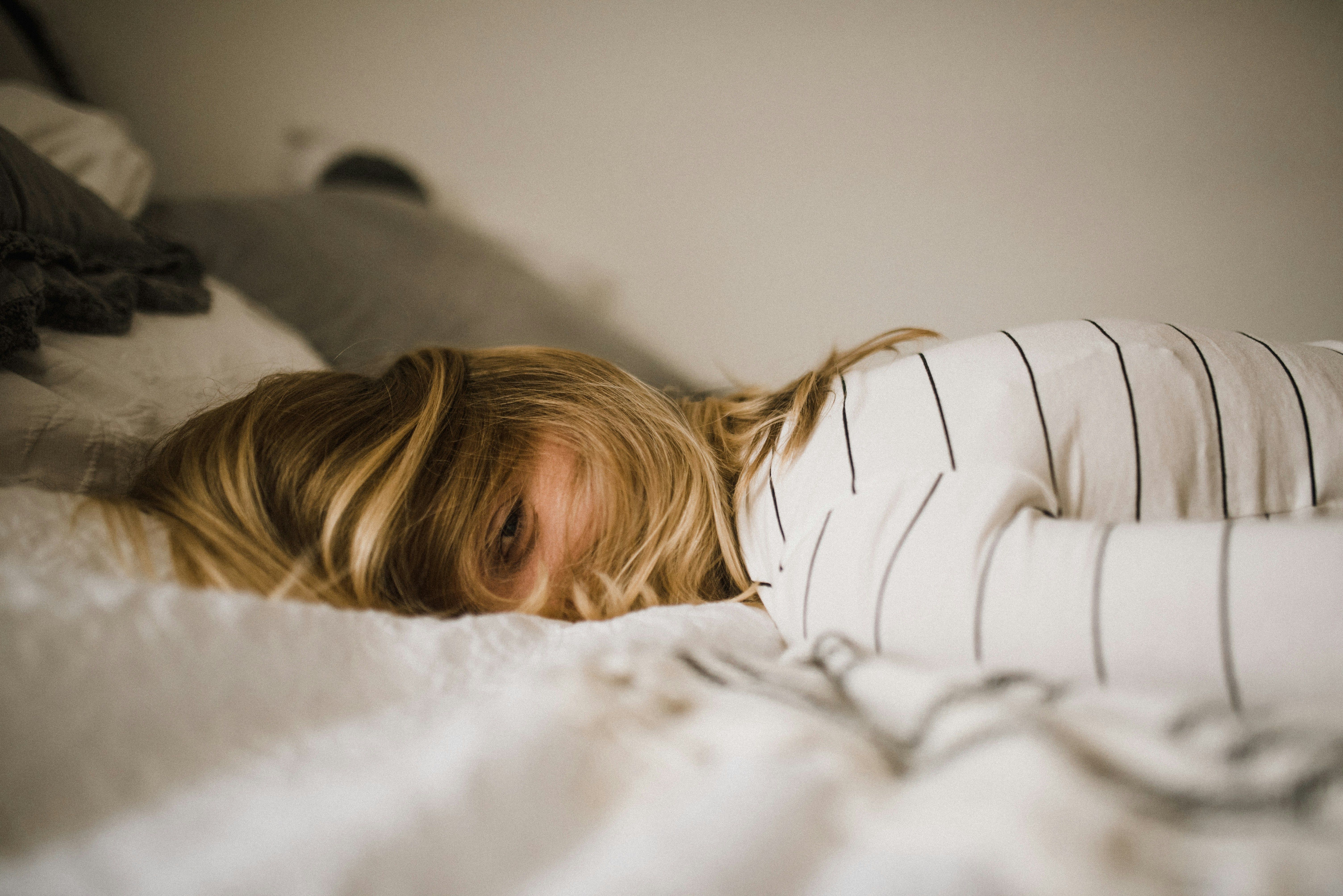 A woman lying on a bed with her eyes open, appearing thoughtful or restless.