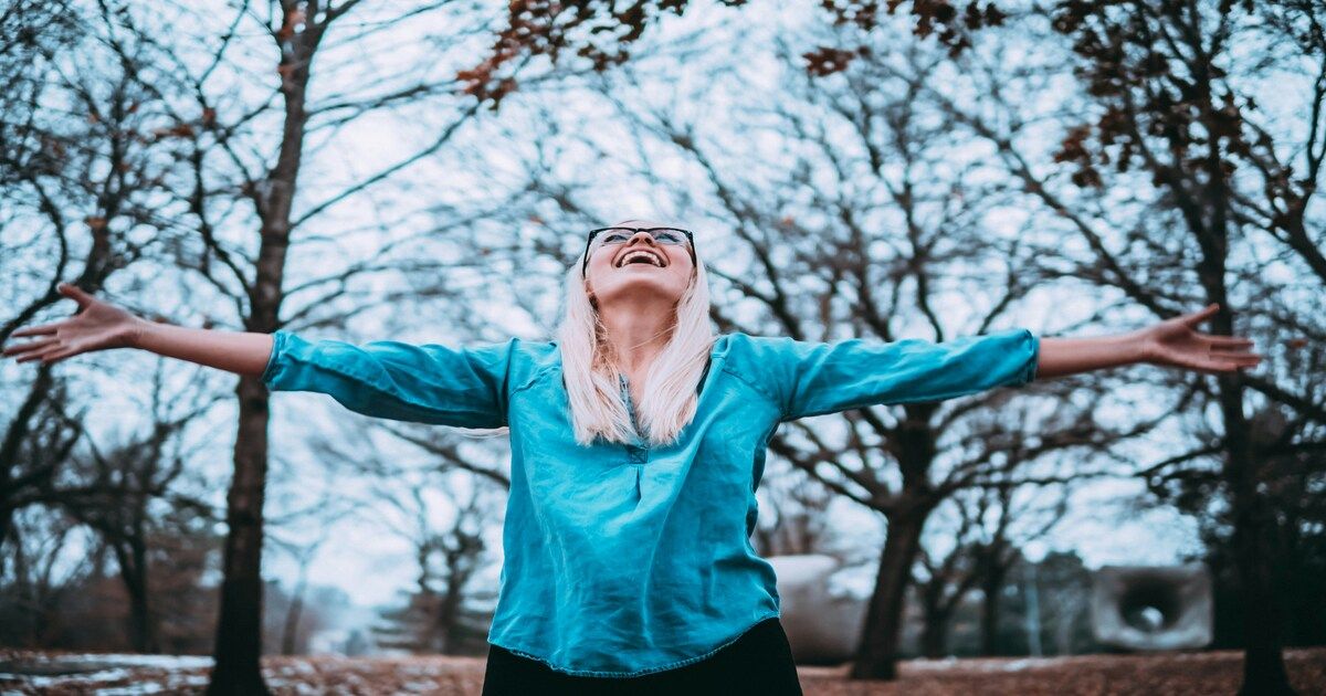 A happy woman raising her hands in the air, representing confidence, self-love, and positive mental health.