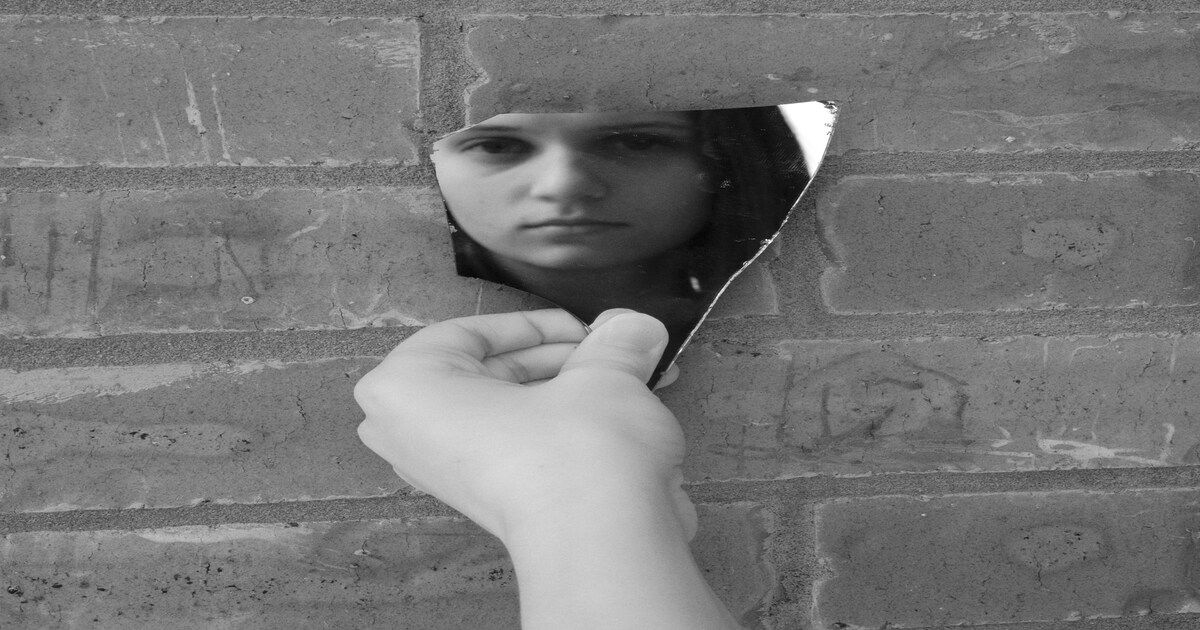 Sad girl looking into a broken mirror, symbolizing the emotional and psychological impact of bullying