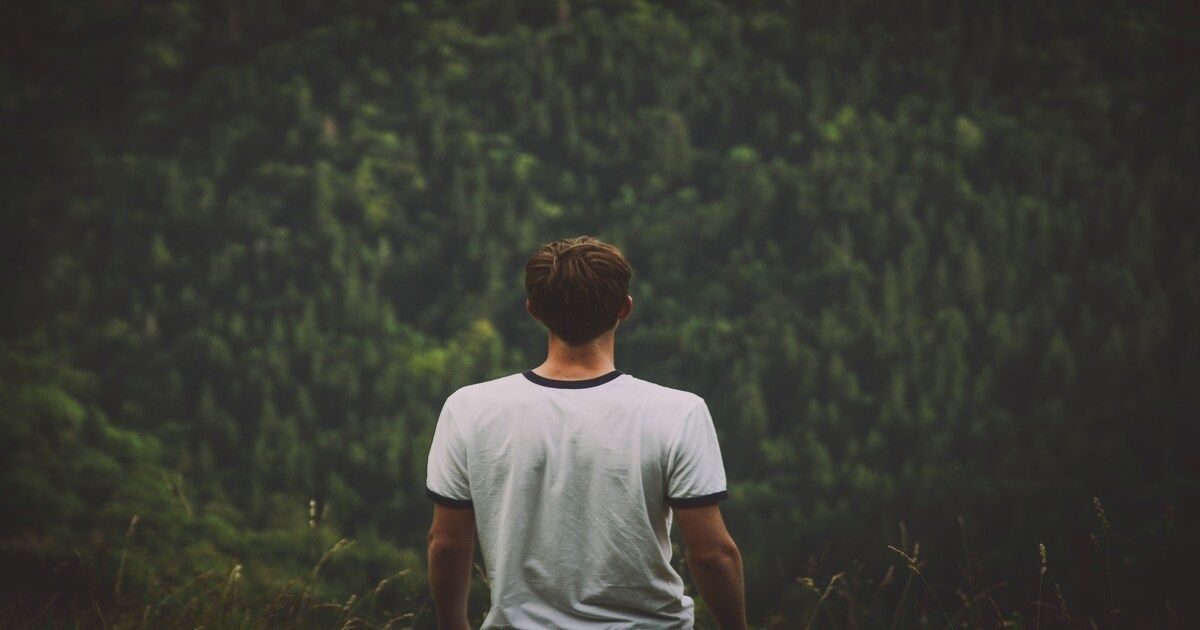 A man standing thoughtfully surrounded by natural scenery.