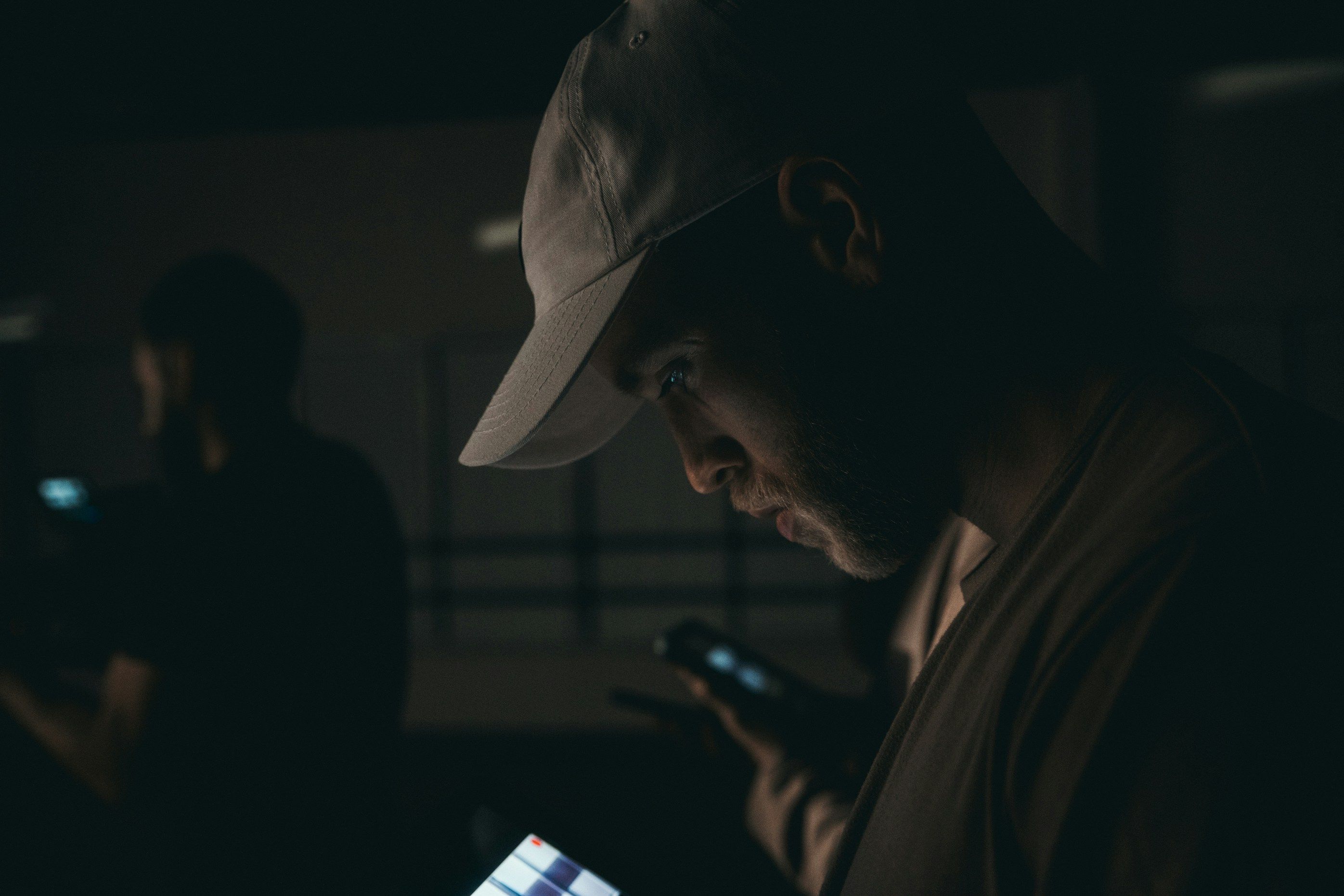 man in cap scrolling phone in dark