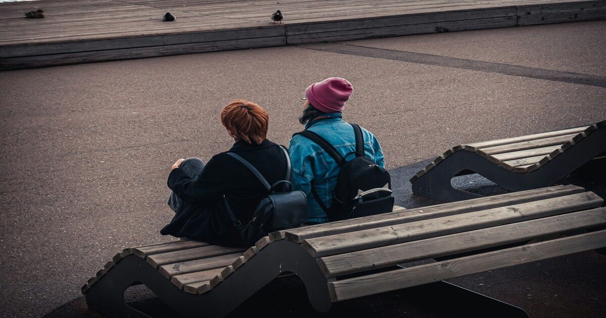 Two women sitting together on a park bench, sharing a quiet moment of support and understanding